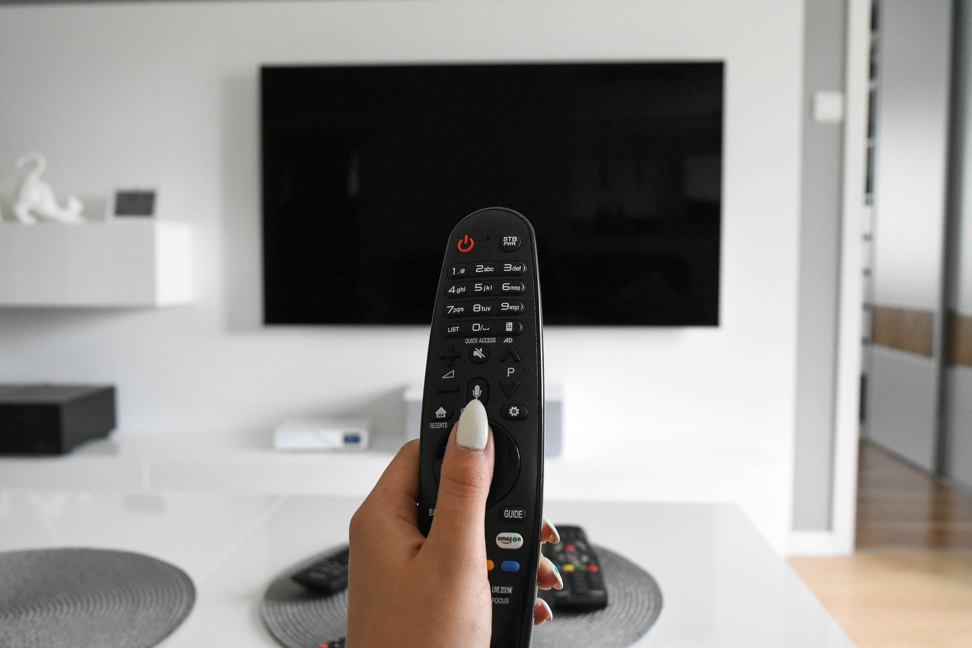 Frauenhand mit Fernbedienung in modernem Wohnzimmer mit grossem TV 