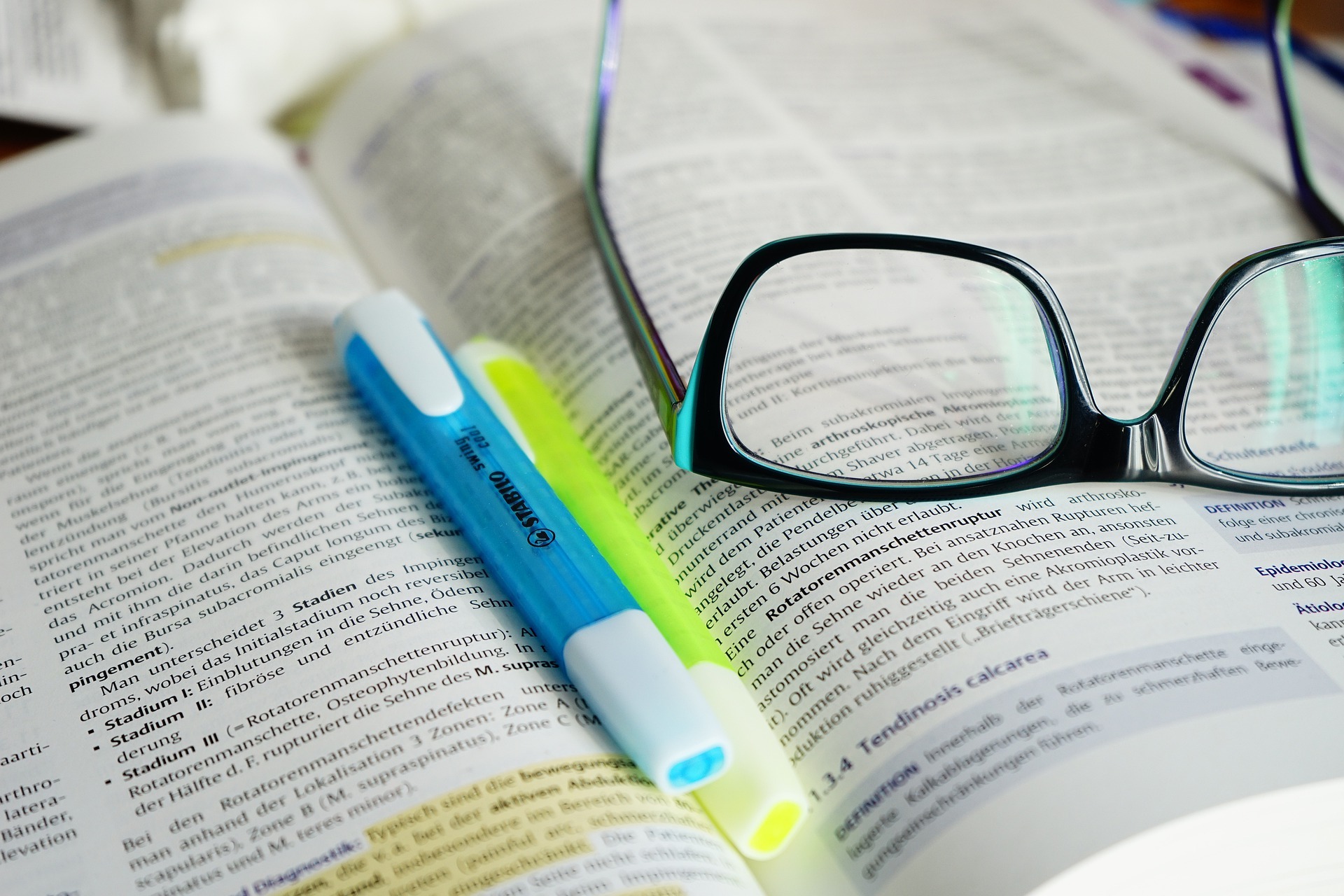 aufgeschlagenes Gesetzestext Buch mit einer Brille und  Textmarkern 